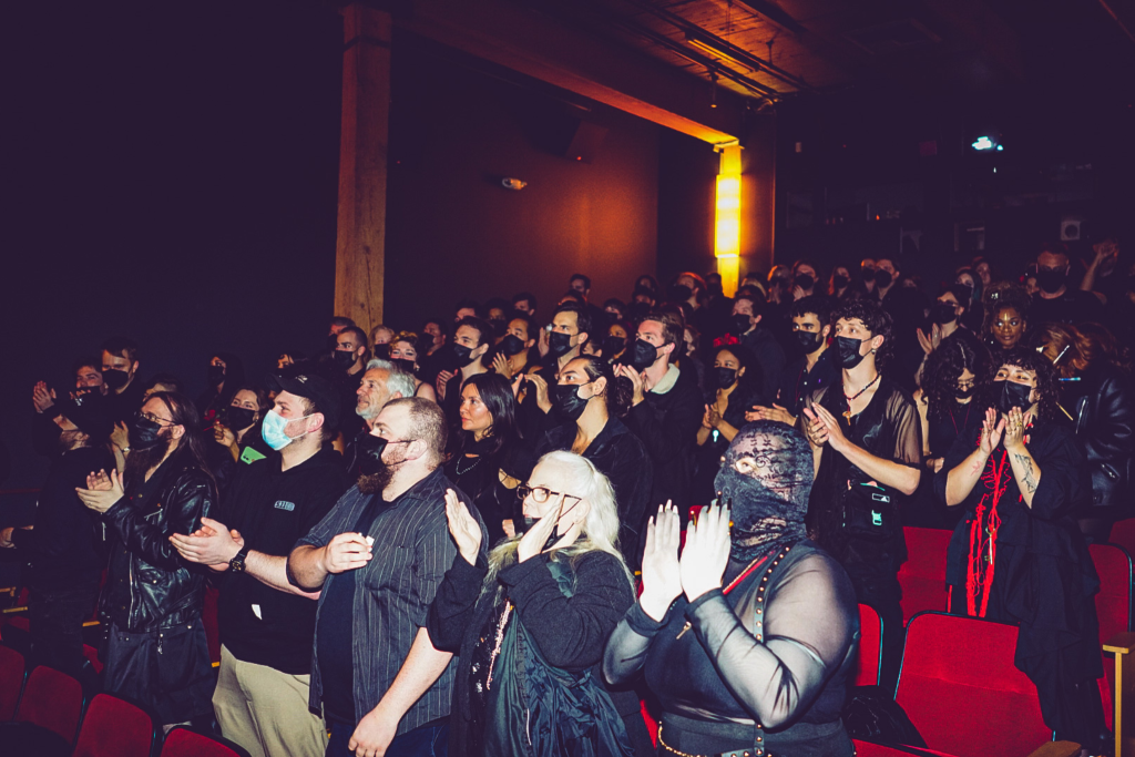 A group of people wearing all black cheering in a dark movie theater.