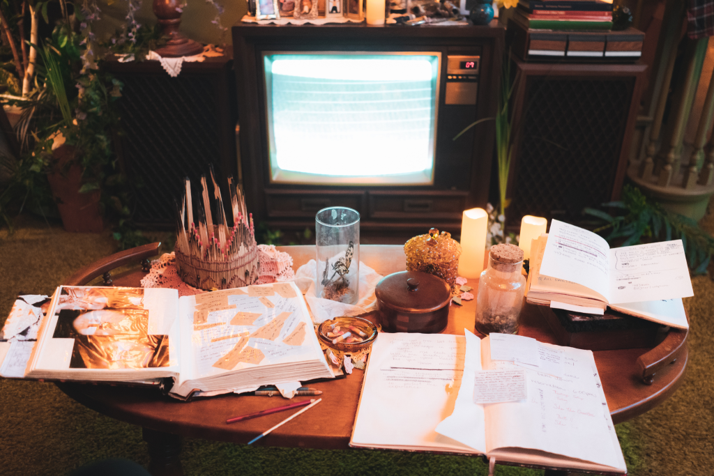 A TV playing a static connection and a table filled open books, candles, glass cups and other items.