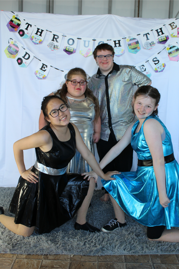 Four young dancers dressed in blue, black, and gold metallic costumes.