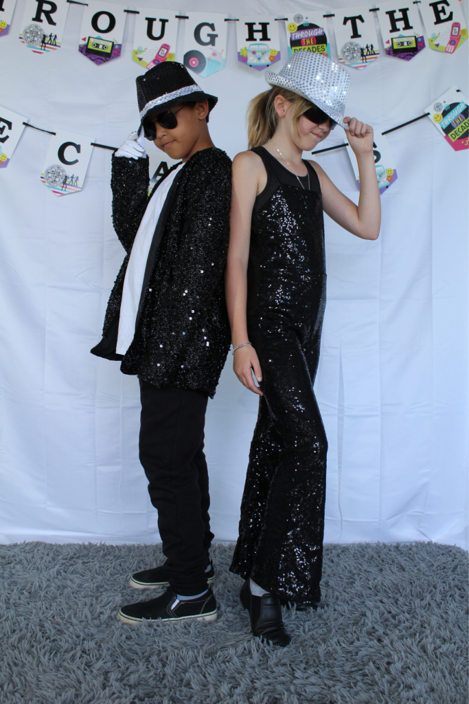 Two dancers dressed in black sequined costumes with fedoras and sunglasses posing for the camera.