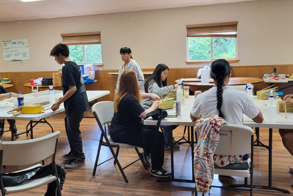 A group of young people, some sitting and some standing, fill the room while working on different projects.