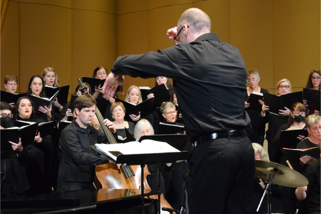 A group of people dressed in black singing. A conductor standing before the choir.