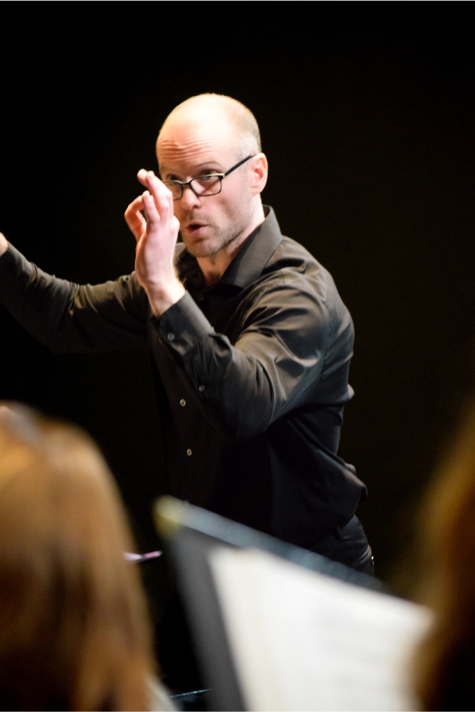 A conductor dressed in black focused on leading the choir.