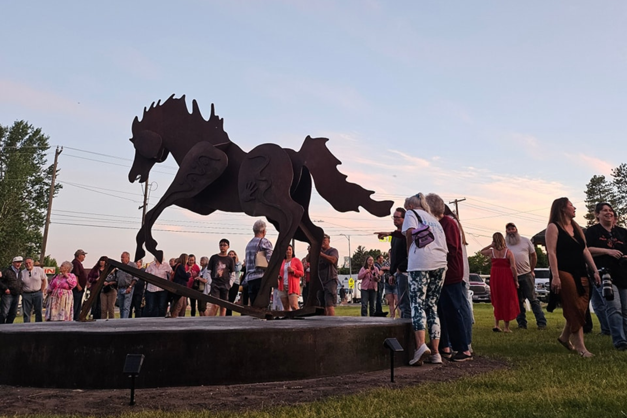 An open outdoor setting filled with people admiring a large horse sculpture.