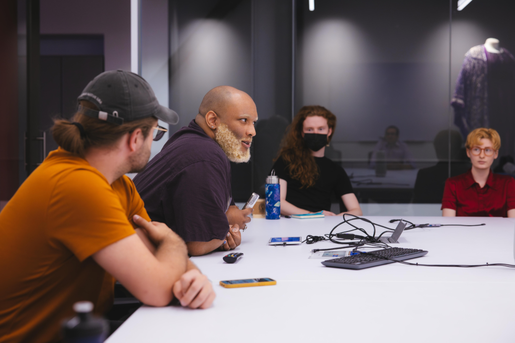 A group of people appear to be discussing topics at a workshop table.