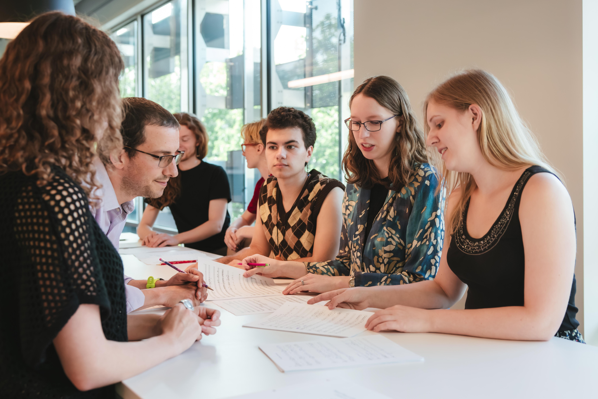 A group of people sitting at a table working together and discussing the sheet of paper that set in front of them.