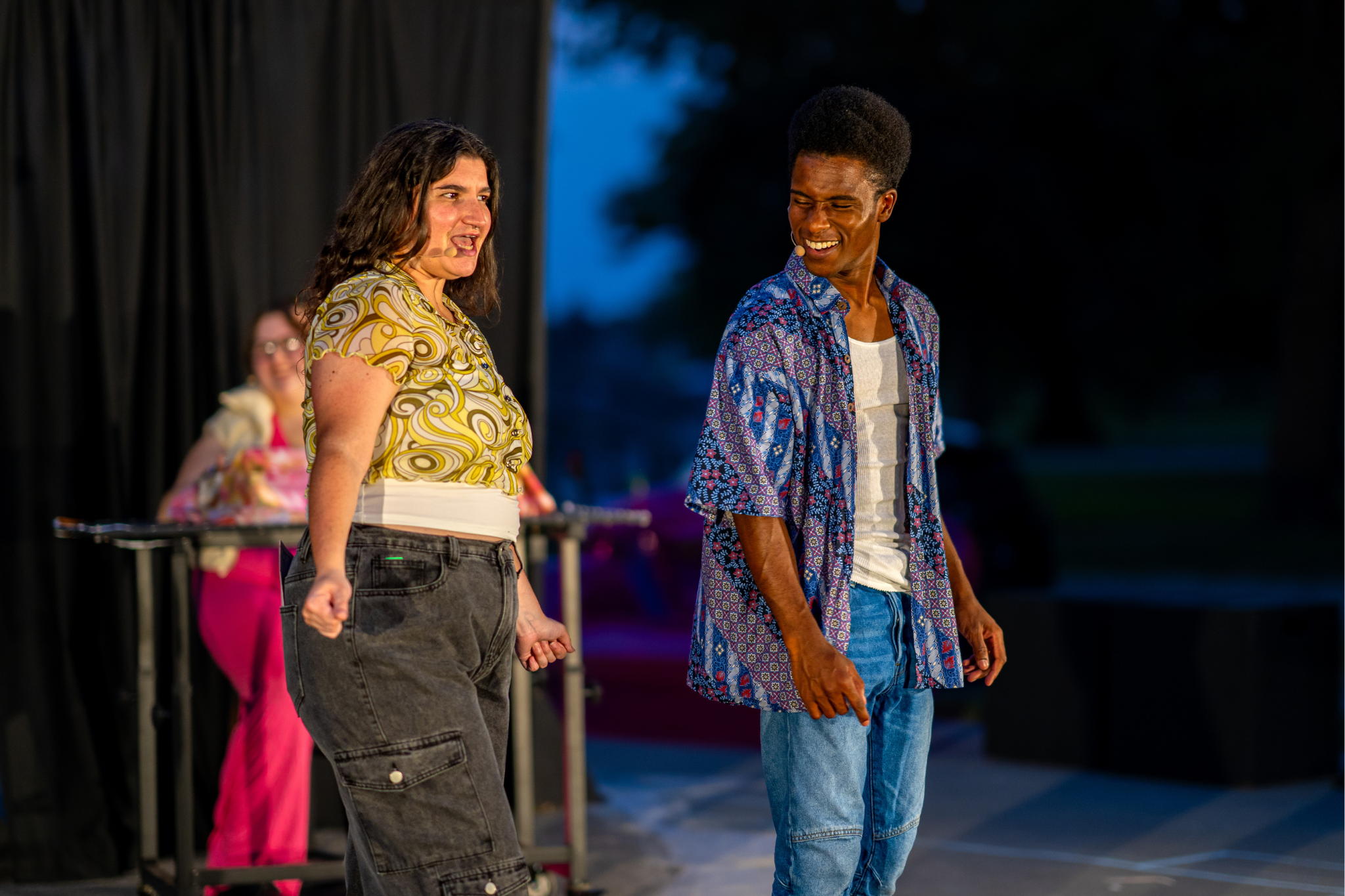 Two characters on a theater stage looking out towards a crowd.