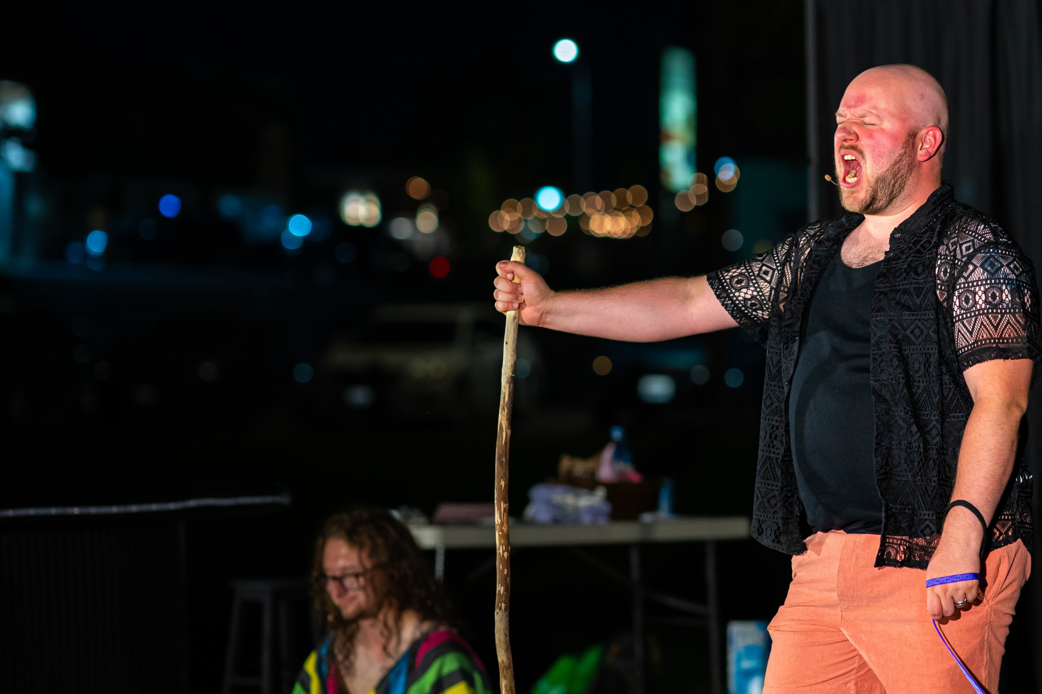 One character on a theater stage with a walking stick, singing enthusiastically towards the crowd.