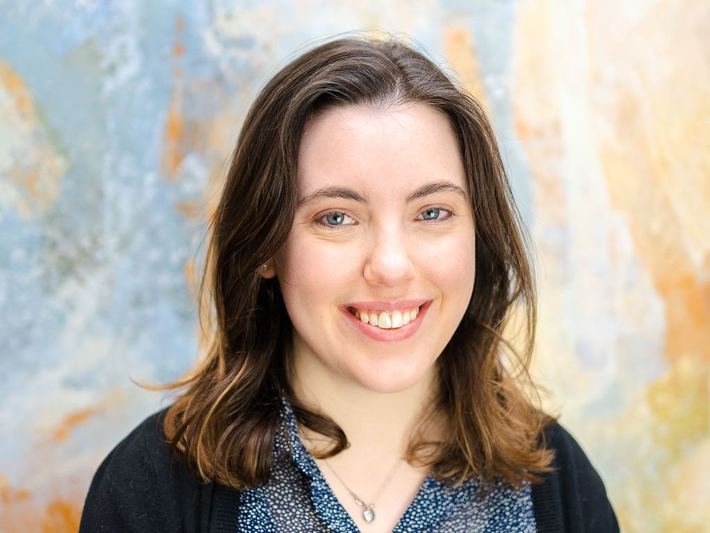 Ellen Milligan of ArtsFund smiles brightly at the camera. She's a brunette with blue eyes and wearing a black cardigan over a blue and white floral shirt.